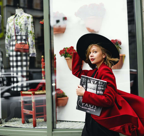 a woman in a red dress holding a magazine standing in front of a store window