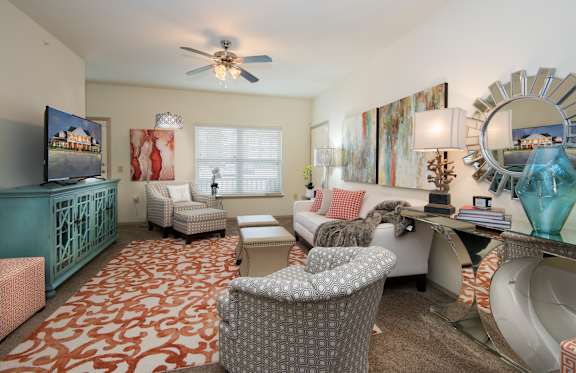 A living room with a patterned carpet and a ceiling fan.
