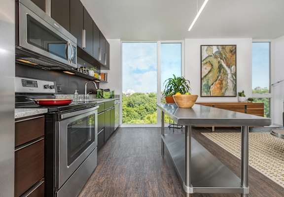 A modern kitchen with stainless steel appliances and a view of the trees outside the window.