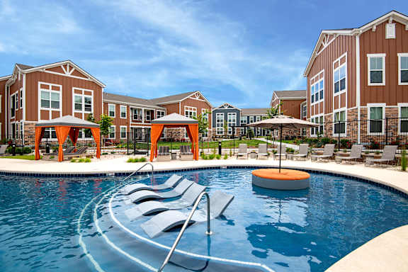 an outdoor pool with chairs and umbrellas in front of an apartment building at Watermark on Twenty Mile, Parker, 80134