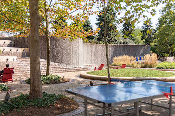 A table tennis table in the middle of a park with trees and benches.
