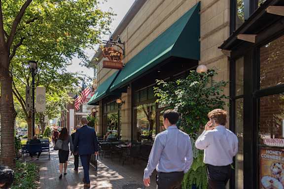 A man in a blue suit walks down a sidewalk past a restaurant with a green awning.