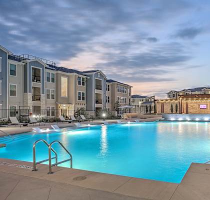 A large swimming pool in front of apartment buildings at dusk.
