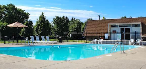 a swimming pool with chairs and a building in the background  at The Wynds, Kettering, OH