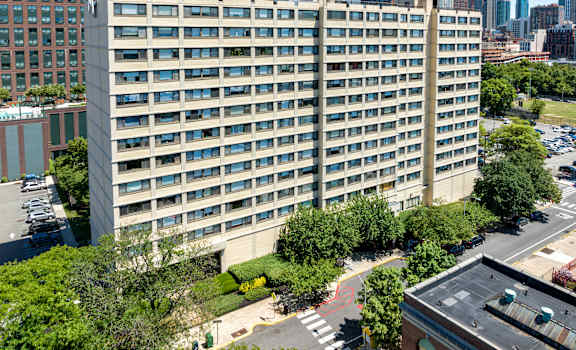A large building with many windows is surrounded by trees and other buildings.