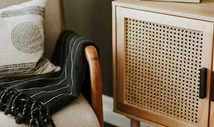 A chair with a pillow and a blanket is next to a cabinet with a vase on top.