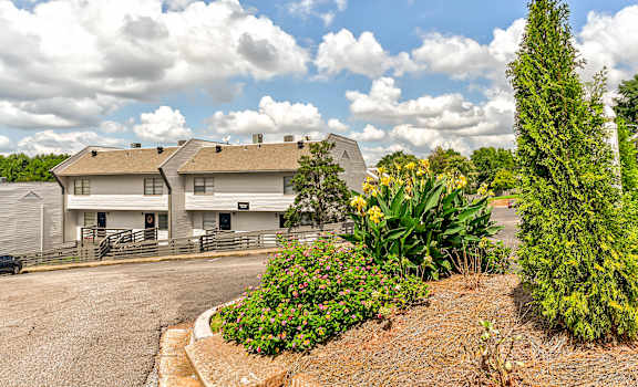 A white building with a grey roof is surrounded by a garden with a variety of plants and flowers.