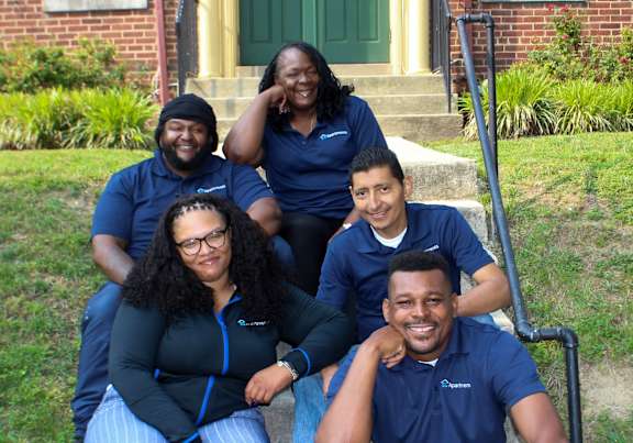 A group of people in blue shirts are sitting on a concrete step outside a house.
