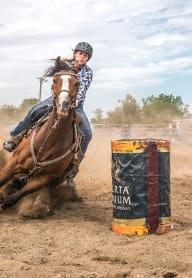 a cowboy riding a horse around a barrel in a rodeo