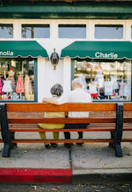 Two people sitting on a bench in front of a store.