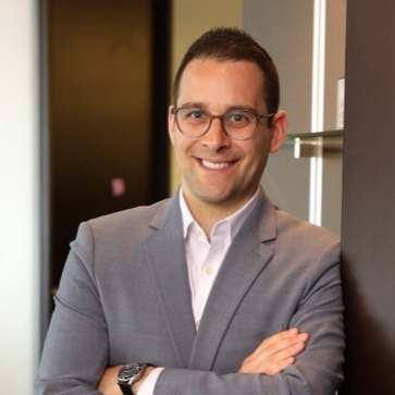 A man in a grey suit and white shirt is smiling.