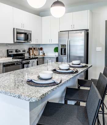 an open kitchen with a marble counter top and a large island with plates and bowls at The Louis Apartment Flats, Louisville, KY