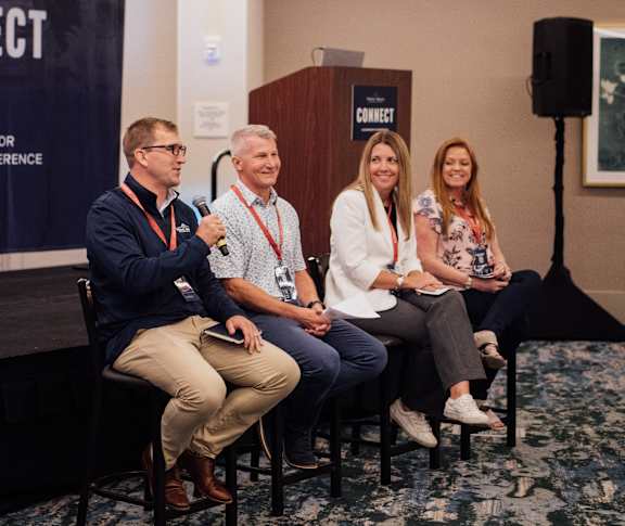 Four people sitting on chairs in front of a podium with a sign that says "CONNECT".