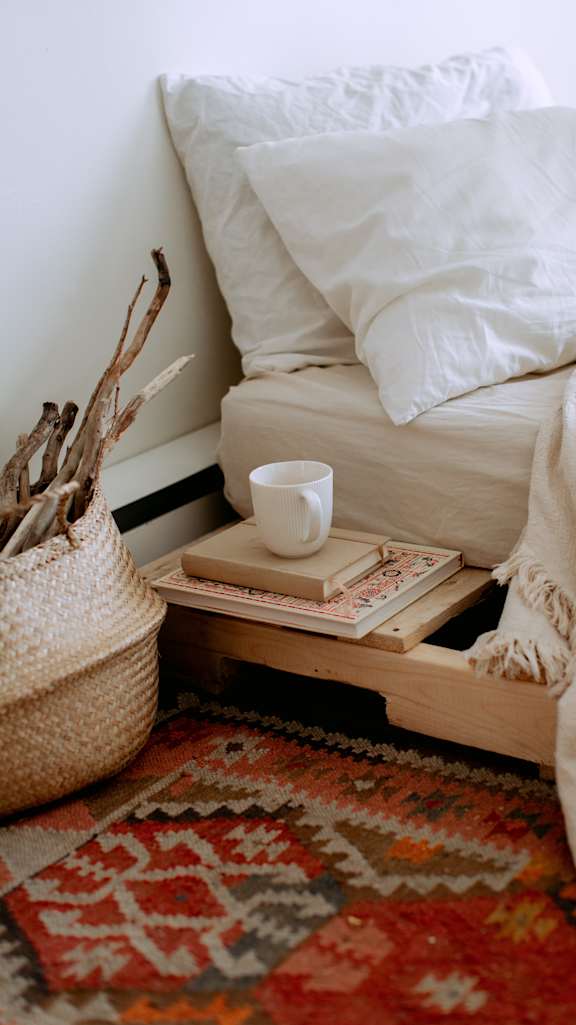 a tray with books and a cup of coffee on it next to a bed
