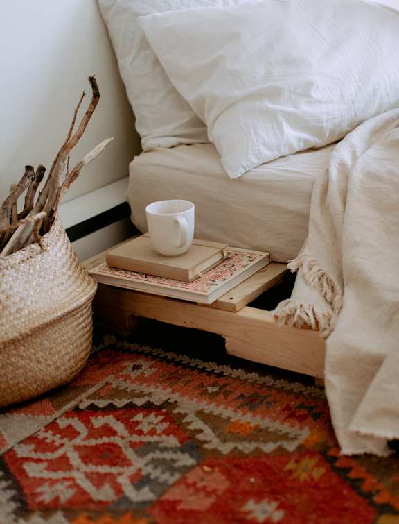 a tray with books and a cup of coffee on it next to a bed