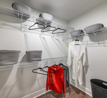 a walk in closet with two wire racks and a white robe and a red jacket