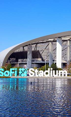 A large stadium with a semi-circular roof and a body of water in the foreground.