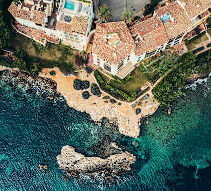 A large rock juts out of the sea in front of a cluster of buildings.