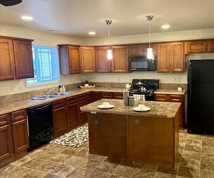 A large kitchen with black appliances, spacious marble countertops, and large wooden cabinets with decorations at Phoenix Ridge Apartments. 