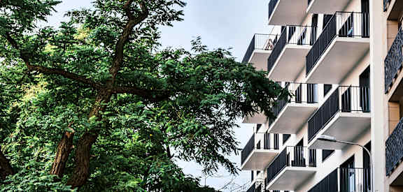 A tall building with balconies is surrounded by trees.
