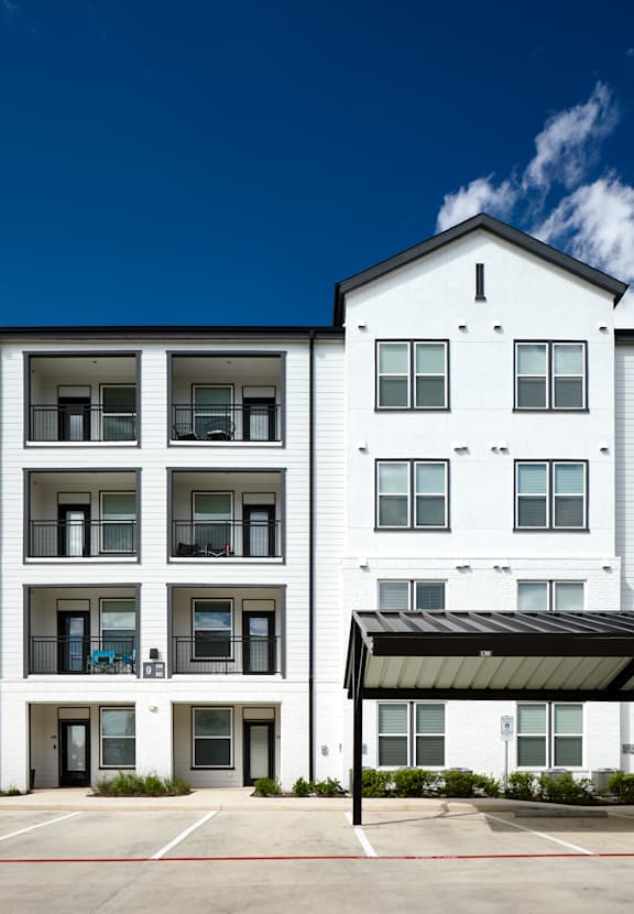 A white building with a black awning sits next to a white building with a black balcony.