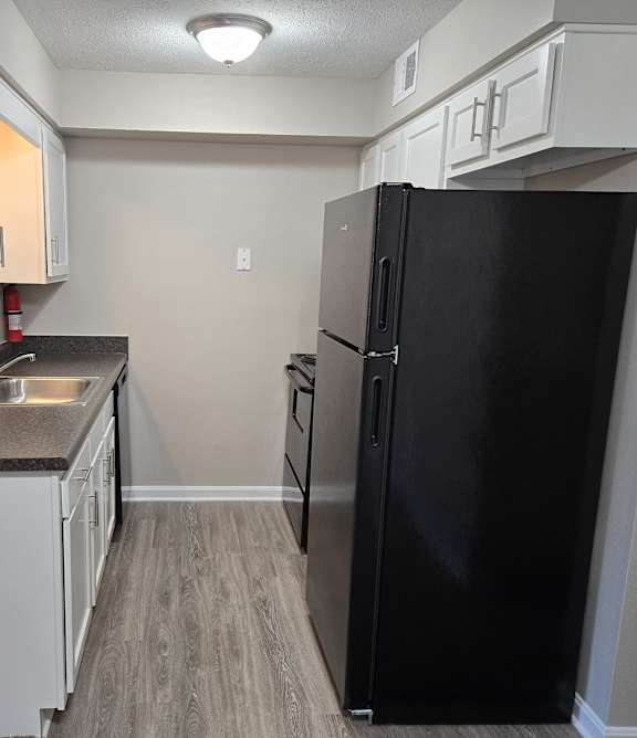 an empty kitchen with a black refrigerator and a sink