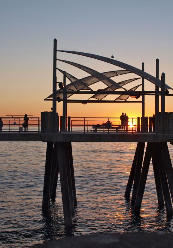 a group of people are standing on a pier at sunset