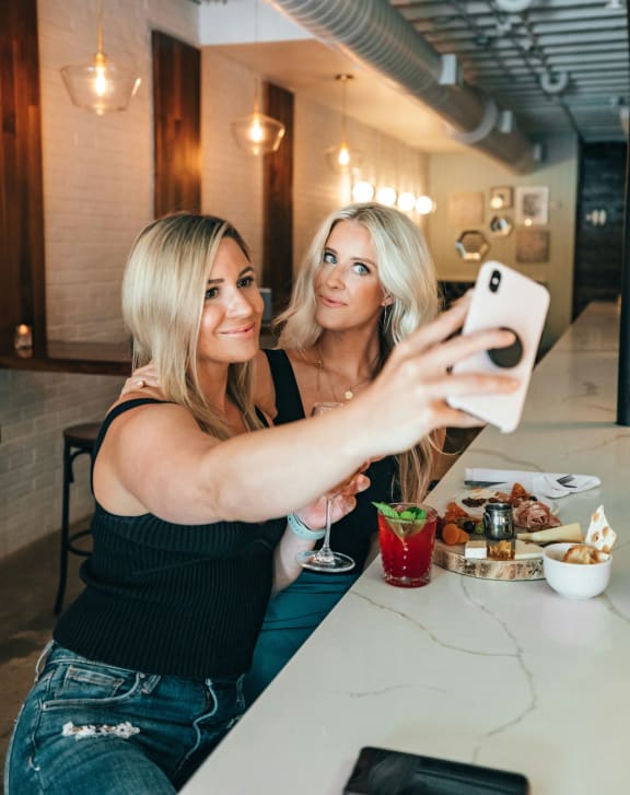 two women sitting at a table taking a picture of themselves in a mirror