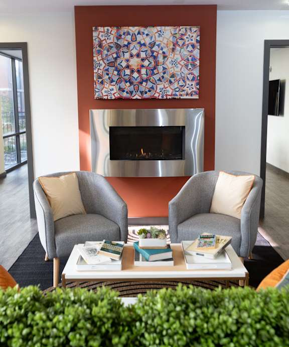 A living room with two grey chairs, a coffee table with books and a fireplace with a painting above it.