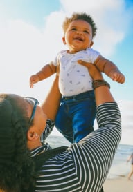 a woman holding a baby up in the air on the beach at Pacific Walk, Washington, 98499