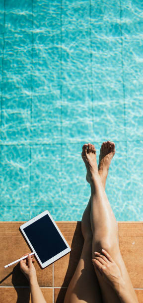 woman laying by the pool with her feet up on a tablet