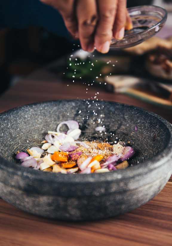 A person is adding spices to a bowl of food.