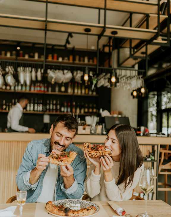 Two people eating pizza in a restaurant.