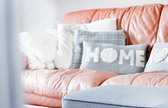 A grey couch with a pillow and a small table with a plant and a picture frame.