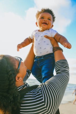 a woman holding a baby up in the air on the beach