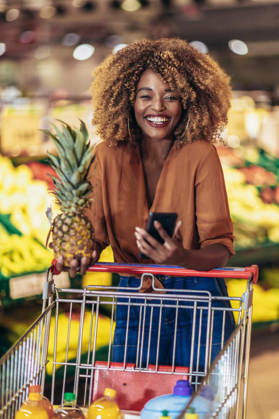 young woman shopping at the supermarket with a cart and holding a pineapple