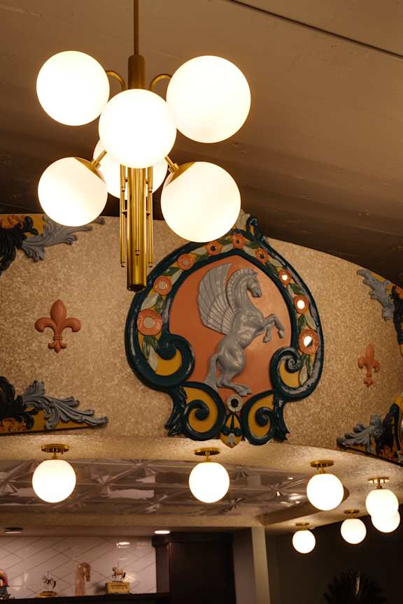 A chandelier with white globes hangs from a ceiling with a decorative mural.