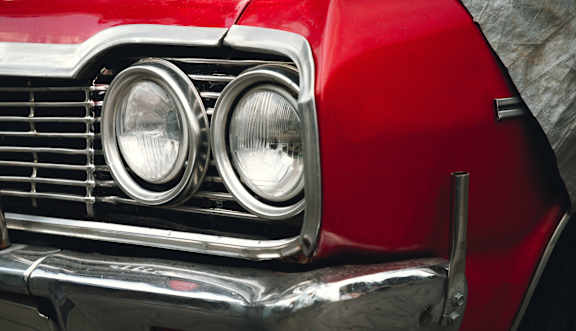 A red vintage car is shown from the front.