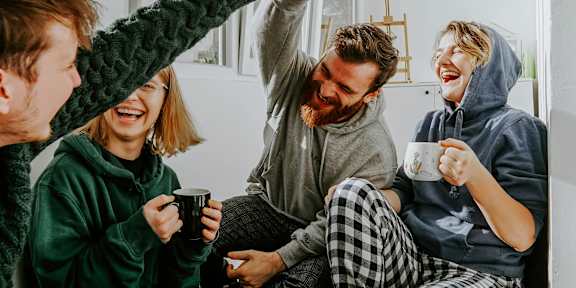 Four people in pajamas are sitting on the floor and high-fiving each other.