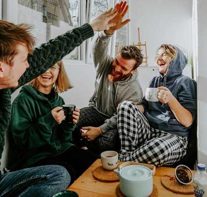 Four people in pajamas are sitting on the floor and high-fiving each other.