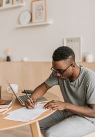 a man sitting at a desk with a laptop and writing on a piece of paper at Cosmopolitan, Seattle, Washington