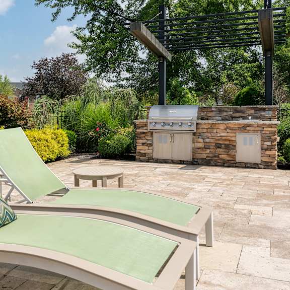 a patio with a grill and two lounge chairs