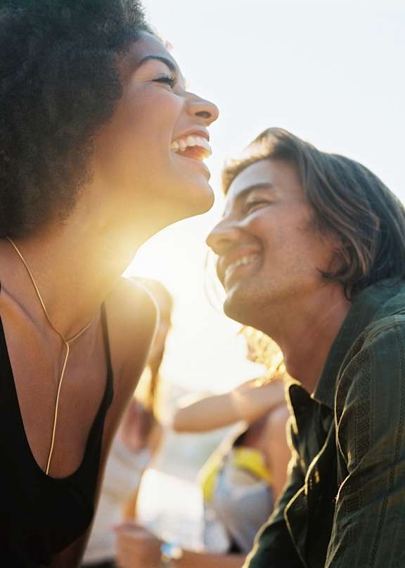 A man and a woman are laughing together in a sunny outdoor setting.
