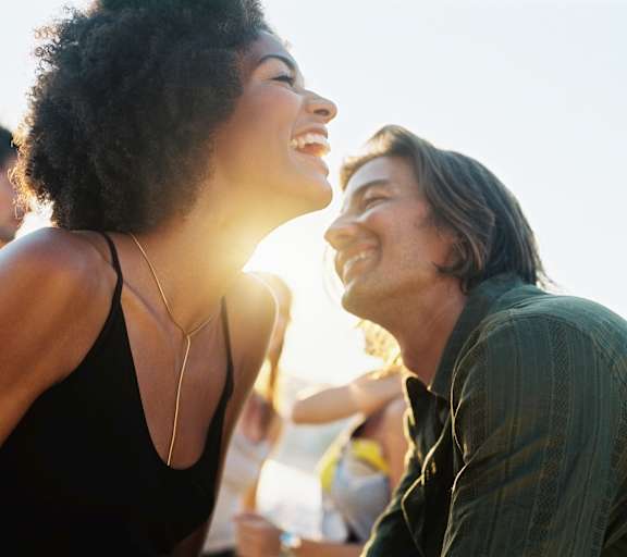 A man and a woman are laughing together in a sunny outdoor setting.