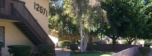 A white picket fence in front of a house with a tree and bushes.