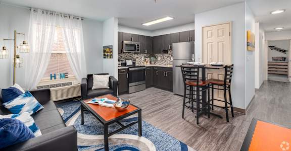 A modern living room with a kitchen area in the background.