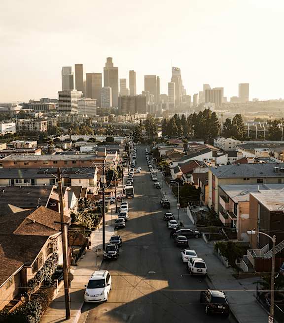 A city street with cars parked on the side and a city skyline in the background.