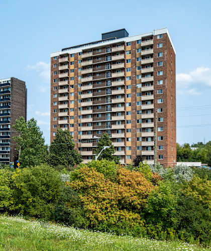 A large brown building with many windows is surrounded by trees and bushes.