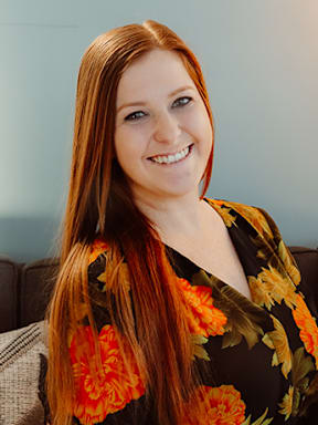 A woman with long red hair wearing a floral dress.
