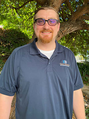 A man with glasses and a beard is wearing a blue polo shirt with a logo on it.
